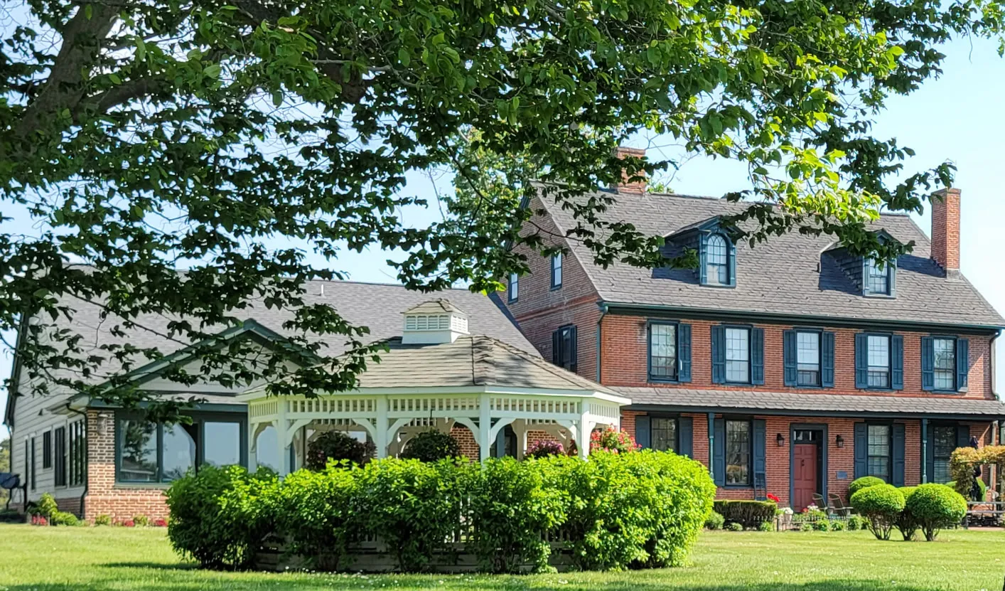 The brick manor house and gazebo framed by shade trees at Joie de Vie Farm